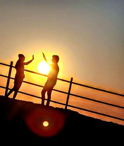 Silhouette people standing by railing against sea during sunset