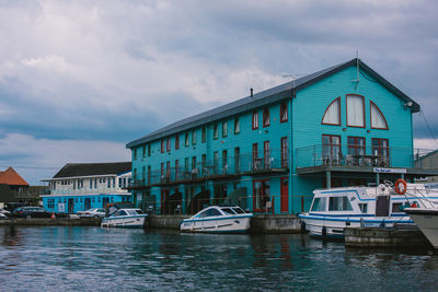 Boats moored in river by buildings against sky
