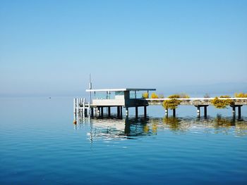 Pier on sea against clear blue sky