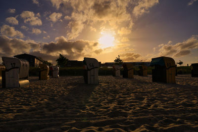 Hooded chairs on beach against sky during sunset