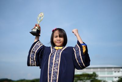 Portrait of confident girl with trophy against sky