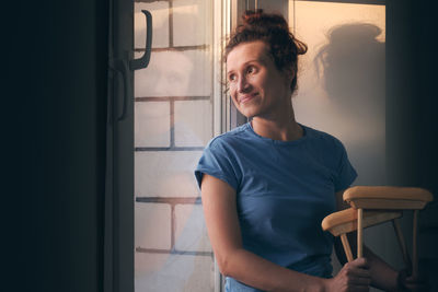 Woman with crutches sits and looks out the window