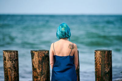 Beautiful blue-haired woman in long dark blue dress with cute tattoo on her shoulder blade on beach