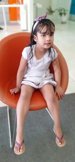 Full length of girl sitting on chair at home