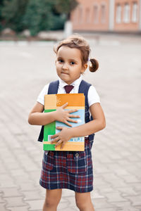 Portrait of cute girl holding book while standing on street