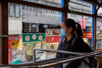 Woman wearing mask looking through window of bus