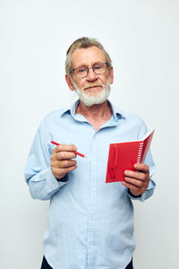 Portrait of man holding book while standing against white background