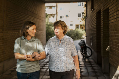 Female nurse talking with elderly female while walking on footpath