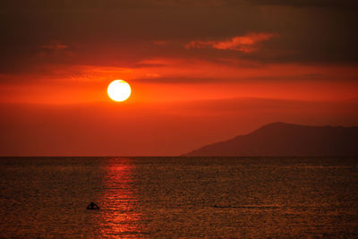 Scenic view of sea against orange sky and silhouette of island