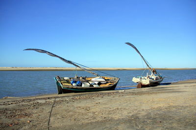 Sailboats moored on sea against clear blue sky