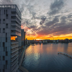 Scenic view of river by buildings against sky during sunset