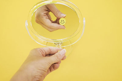 Cropped hand of woman holding bottle against yellow background