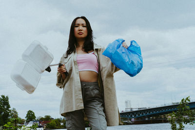 Low angle portrait of confident woman picking garbage near river