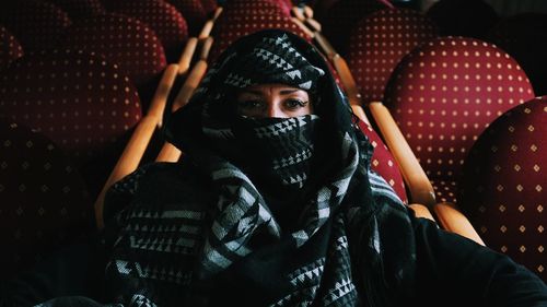 Portrait of woman with covered face sitting on chair