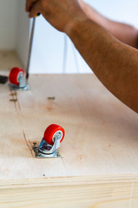 Close-up of electrical screwdriver fixing castor wheel on a wooden table.