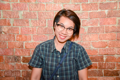 Portrait of smiling young woman against brick wall