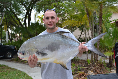 Portrait of man holding large fish against trees