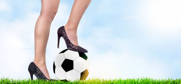 Low section of person playing soccer on grass against sky