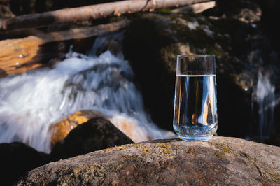 Pure water in a transparent glass against the backdrop of a mountain river in the background