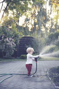 Full length of cute girl holding garden hose