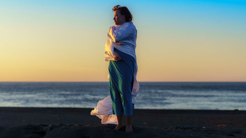 Woman standing at beach against sky during sunset