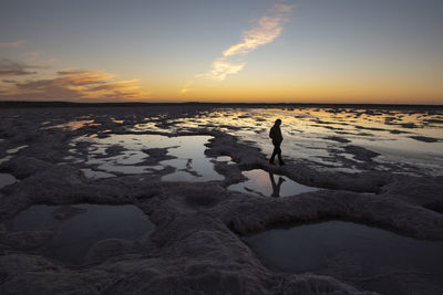 Silhouette of a person walking through a saltworks area at sunset
