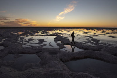 Silhouette of a person walking through a saltworks area at sunset