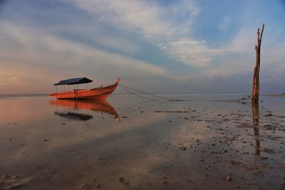 Fishing boat moored at beach against sky during sunset