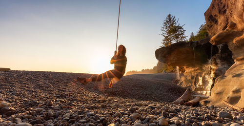 Man on rocks against clear sky during sunset