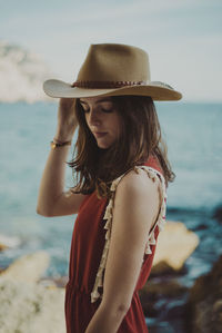 Young woman wearing hat with eyes closed standing against sky