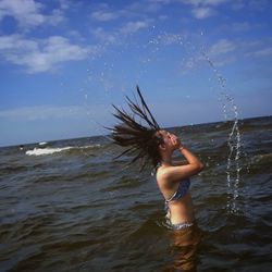 Young woman splashing water in sea against sky