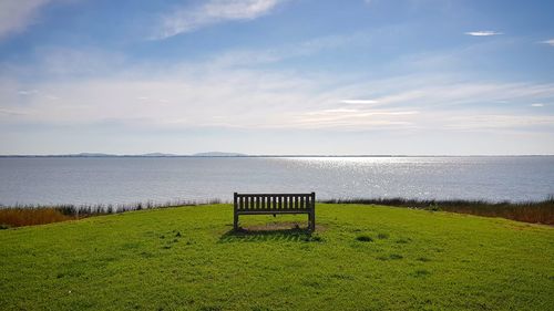 Scenic view of field by sea against sky