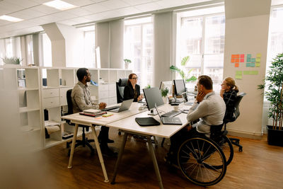 Business colleagues with disabled sales manager working at desk in office