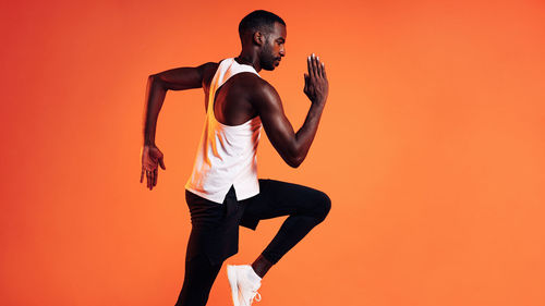 Side view of man running against orange background