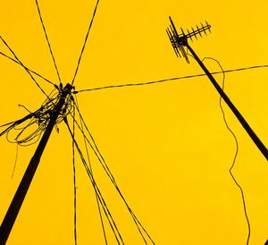 Low angle view of silhouette electricity pylon and antenna against yellow sky