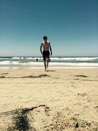 Shirtless teenage boy walking at sandy beach