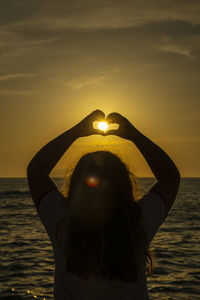 Woman standing by sea against sky during sunset