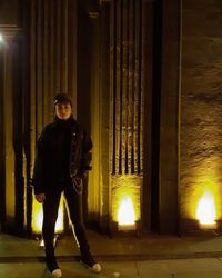 Portrait of woman standing on footpath by illuminated lights at night