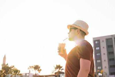 Man wearing hat standing by glass against sky