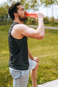 Side view of man drinking water standing at park