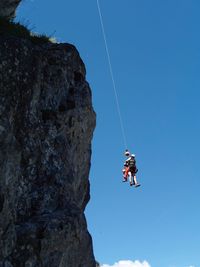 Low angle view of people hanging from rope against blue sky