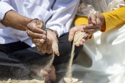 Midsection of people pouring sand on ground