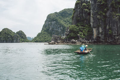 People rowing boat at halong bay by mountains