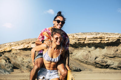 Woman piggybacking man against sky