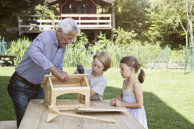 Grandfather and grandchildren building up a birdhouse