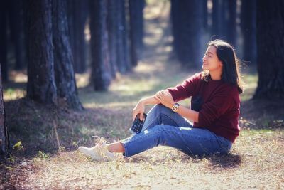 Young woman sitting on tree trunk in forest