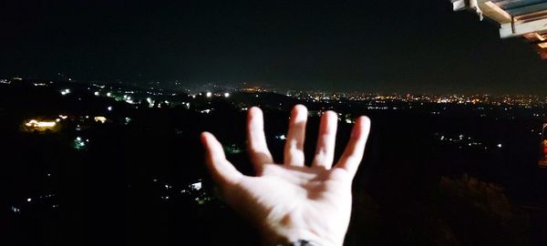 Midsection of person against illuminated cityscape against sky at night