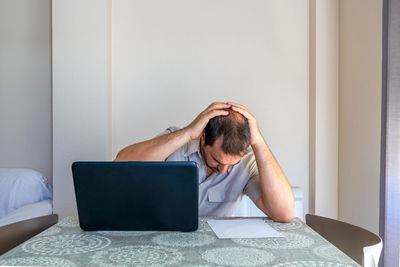 Frustrated man using laptop sitting at home