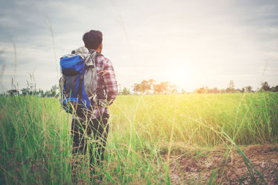 Rear view of backpacker standing on field against sky