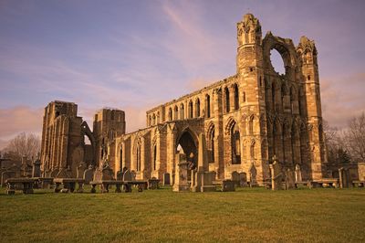 Elgin cathedral by cemetery against sky during sunset